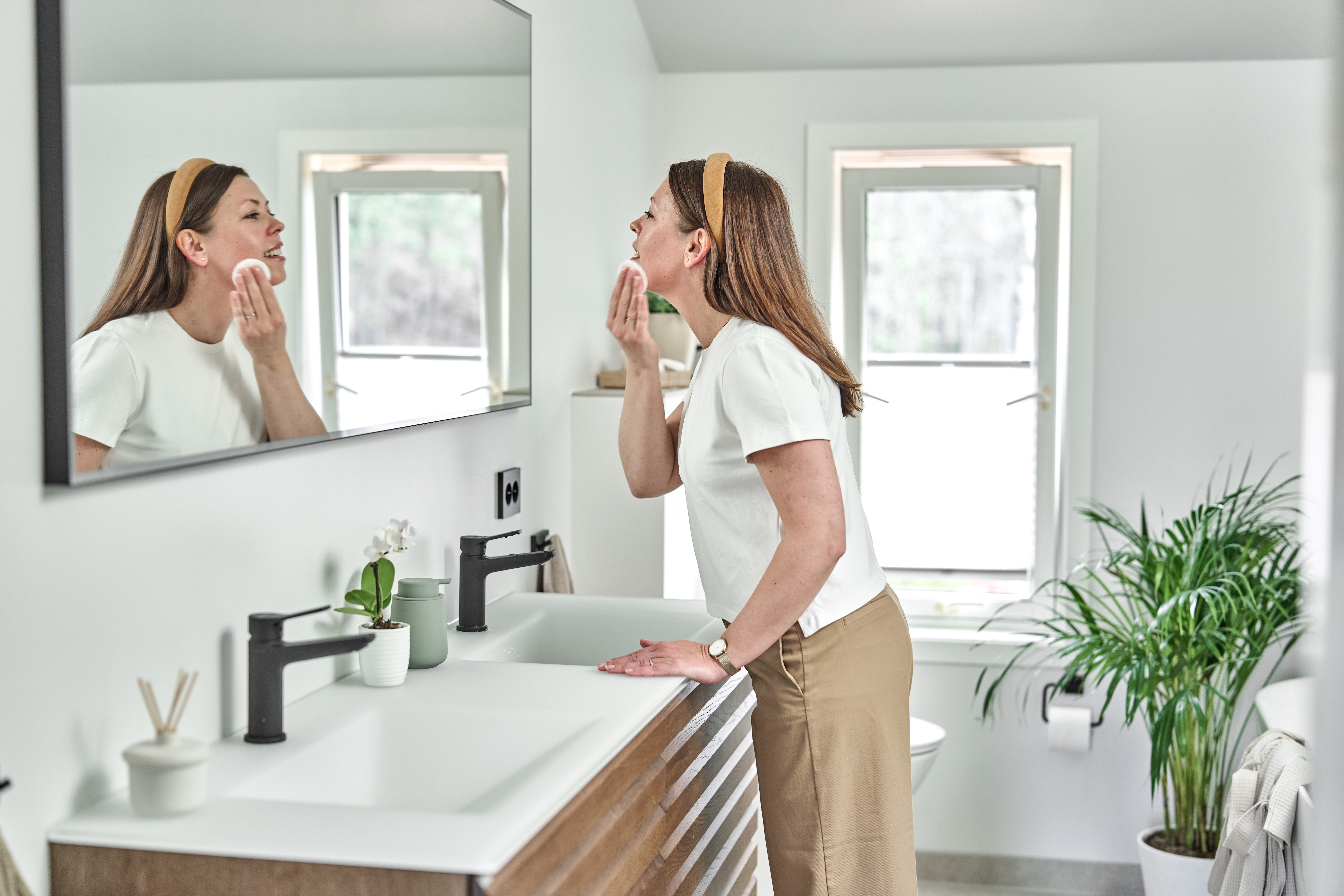 Kvinne står foran speilet på badet og sminker seg.